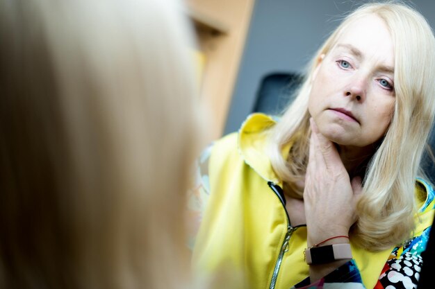 Portrait of middleaged woman looking at her face in mirror skin\
aging concept