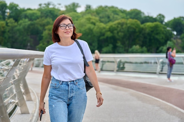 Portrait of middleaged woman walking with smartphone in hand summer day in city