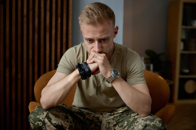 Portrait of military man being deep in thoughts feeling sorrowful and loneliness sitting on chair at psychologist office. Mental disorder and ptsd symptom