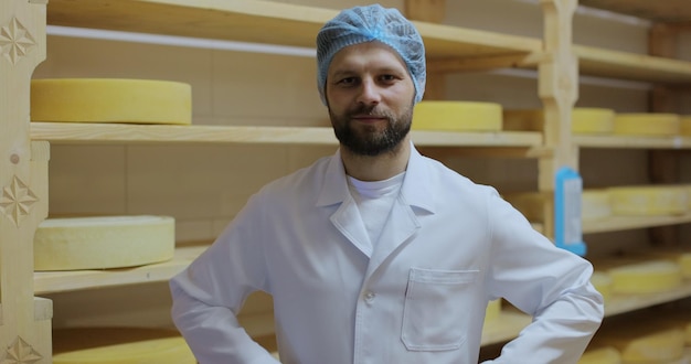 Portrait of milky farmer in a white coat smiling looking at camera with tasty fresh cheese rounds on background Ecologically friendly products