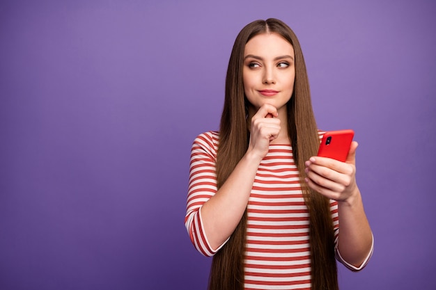 Portrait minded cunning curious girl use smartphone look copyspace touch chin hand plan write incredible followers subscribers liking post wear white jumper isolated violet color wall