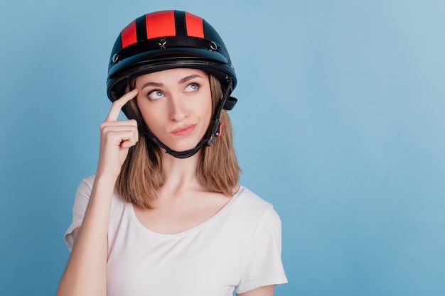 Ritratto di una donna motociclista dubbiosa che indossa un casco da motociclista sembra uno spazio vuoto pensa su sfondo blu