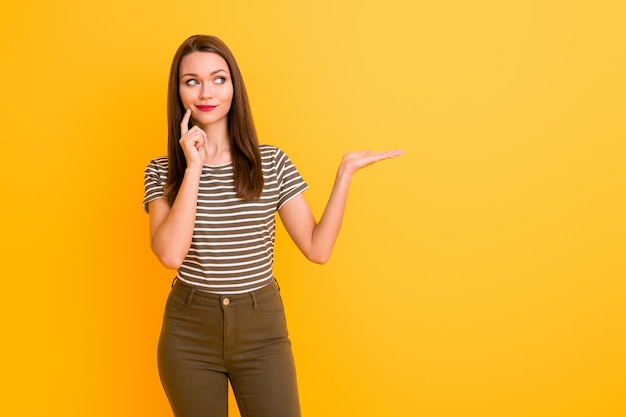 Portrait of minded girl promoter hold hand think thoughts dilemma what promotion adverts recommend display select suggest present wear white green outfit isolated yellow color wall