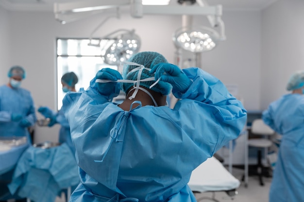 Portrait of mixed race male surgeon in operating theatre putting on face mask