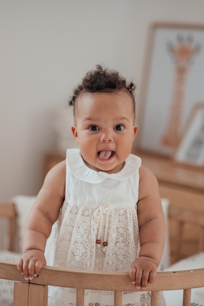 Portrait of mixed race toddler girl in round wooden baby crib at cozy childrens room neutral tones