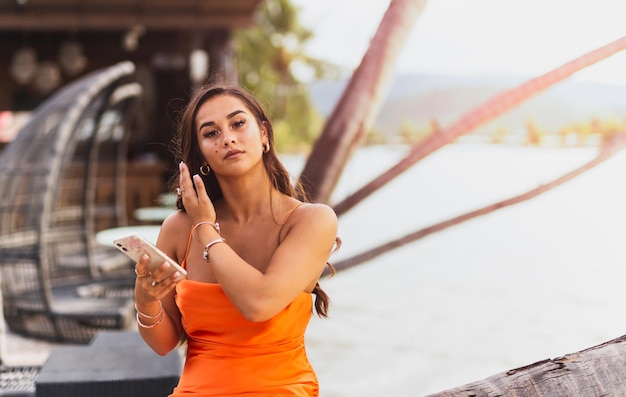 Portrait of mixed race woman in orange dress holding cell phone