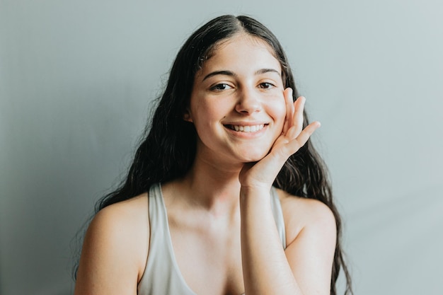 Portrait of model with hand in face relaxed after dermatology skin treatment Young adult woman skincare glow from spa rituals posing with glowing clean and clear skin and no makeup