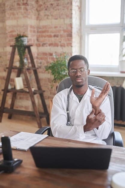 Портрет современного африканского врача-американца, сидящего в кабинете на чердаке и проверяющего частоту сердечных сокращений на ок.