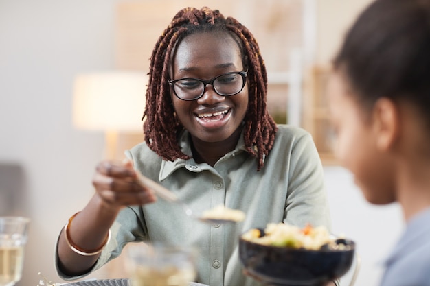 家で一緒に夕食を楽しんでいる現代のアフリカ系アメリカ人の家族の肖像画、娘と自家製の食事を共有する笑顔の若い女性に焦点を当てる