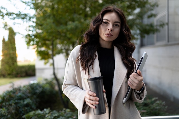 Ritratto di una donna d'affari moderna con un computer portatile e un bicchiere di caffè in mano contro