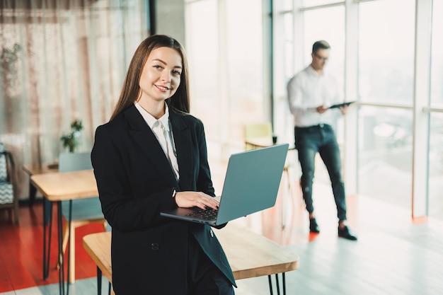 Portrait of a modern business woman with a laptop in the office A business woman in a black classic suit who works online in the office