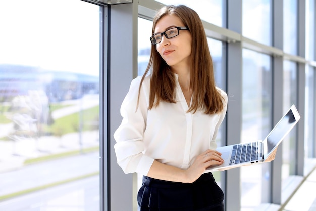 オフィスのコピースペースエリアでラップトップコンピューターで作業している現代のビジネス女性の肖像画