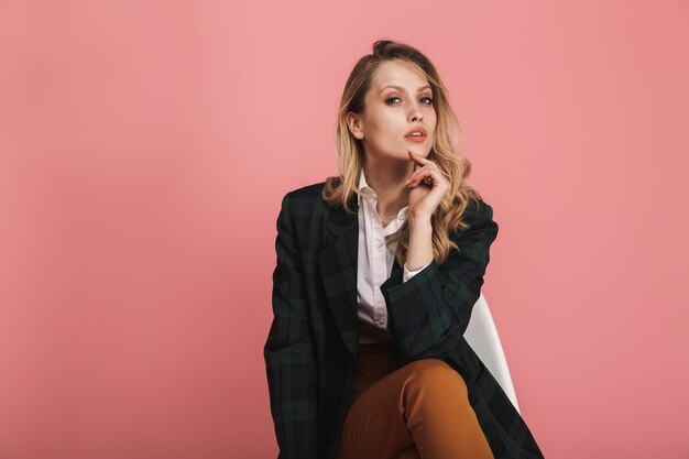 Portrait of modern businesswoman wearing jacket sitting in chair isolated on pink