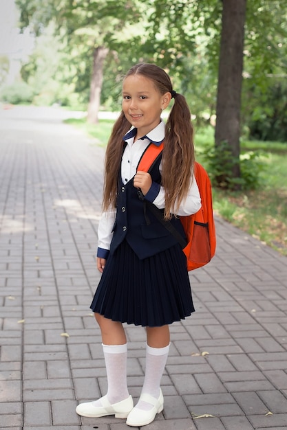 Portrait of a modern happy schoolgirl-child with a backpack bag in the park. The girl smiles and looks at the camera.