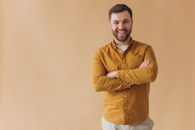 Foto ritratto di un uomo barbuto millenario moderno felice e sorridente con una camicia gialla su uno sfondo beige