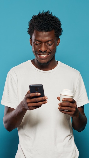 Portrait of modern person looking at display on smartphone. Cheerful man using mobile phone with touchscreen, feeling charismatic. Adult holding device with technology in studio.