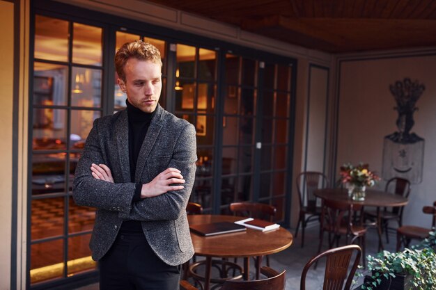 Portrait of modern young guy in formal clothes that stands in the cafe.