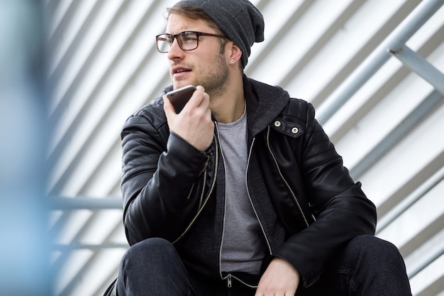 Portrait of modern young man talking on the phone with hands free in the street.