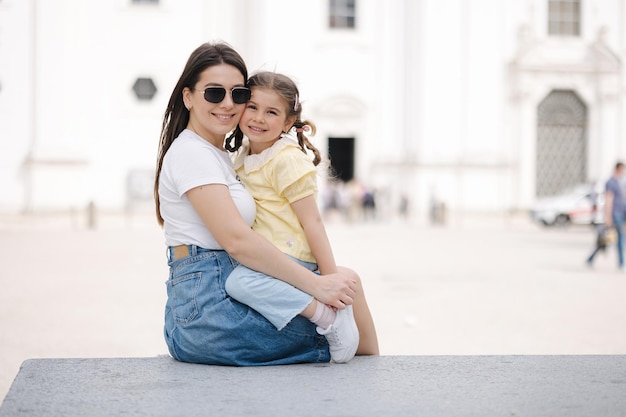 Portrait of mom and daughter sits on stone bench and hug each other