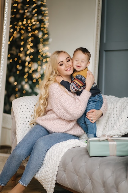 Portrait of mom and son sitting on a coach at home near the Christmas tree, all are smiling. Christmas family. Happiness.