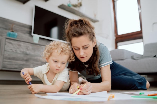 Portrait of mom with her preschoolaged daughter spending their\
free time drawing together while lyin