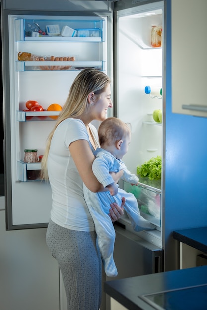 Portrait of mother and baby son looking for something to eat in the refrigerator at night