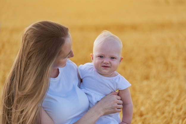 Portrait of mother and child on background of wheat field. Cute baby and young mom. Happy childhood