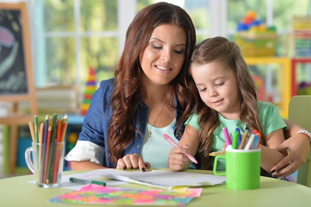 Portrait of mother and daughter drawing together with felt pens at playroom