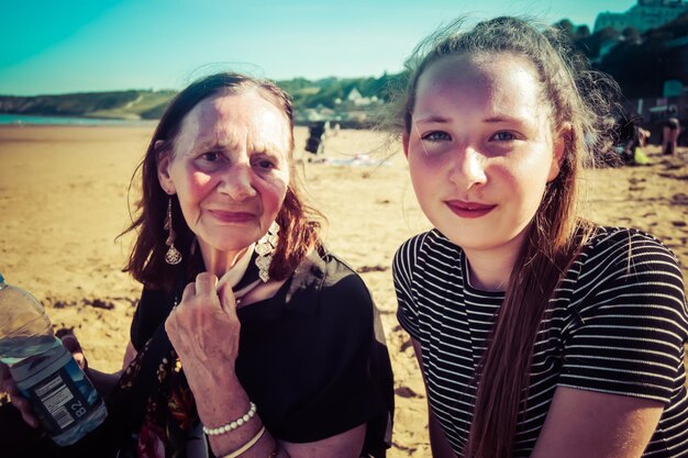 Photo portrait of mother and daughter sitting at beach against clear sky