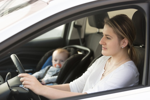 Portrait of mother driving car with her baby sitting on front seat