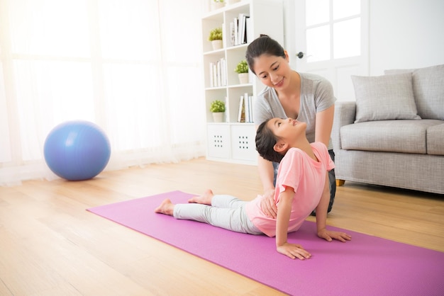 Ritratto di madre che insegna delicatamente alla sua bambina le sue prime nozioni di yoga attento vicino al corpo dei bambini che aiuta la figlia a finire l'azione nella lezione di fitness a scuola.