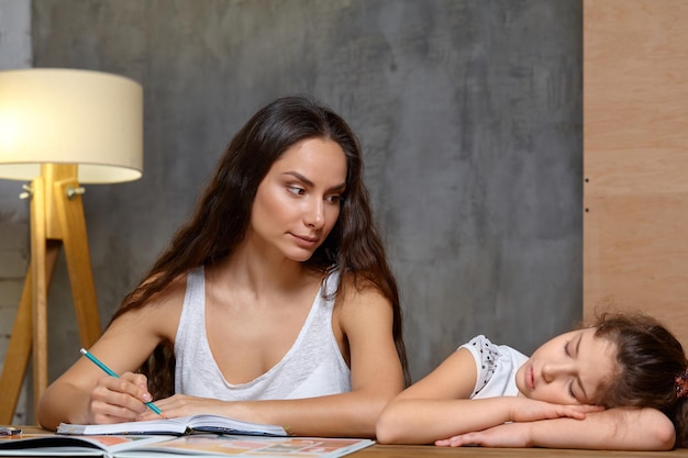 Portrait of a mother helping her small sweet and cute daughter to make her homework indoors. Happy family.