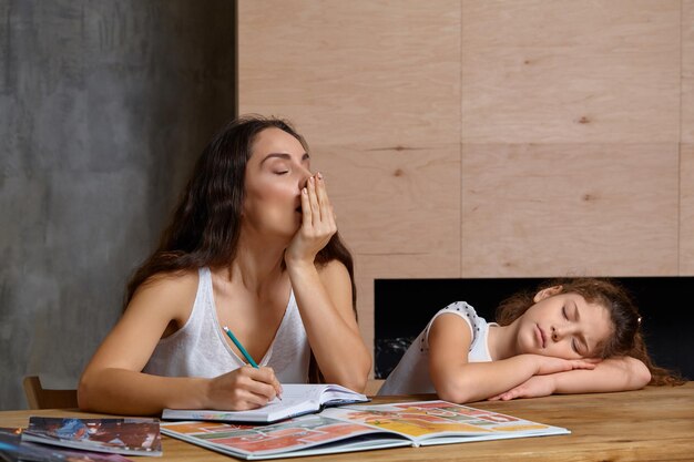 Portrait of a mother helping her small sweet and cute daughter to make her homework indoors. Happy family.