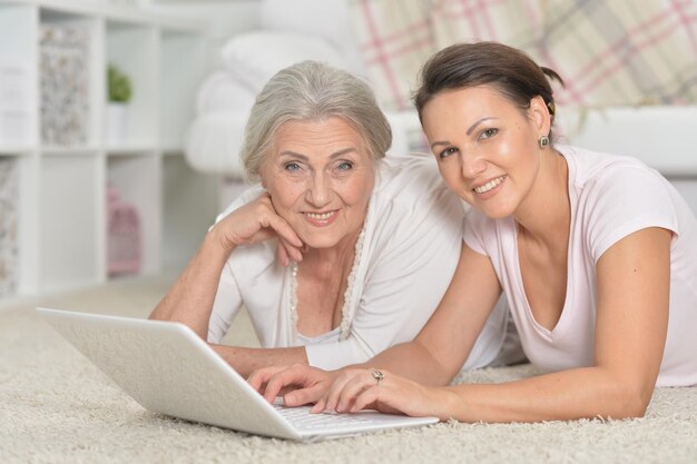 Portrait of mother and her adult daughter lying on floor and using laptop