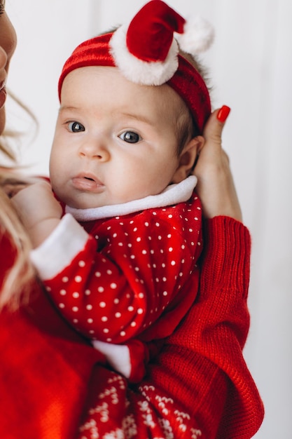 Portrait of mother and little daughter in traditional Christmas clothes in light wooden room near window copy space