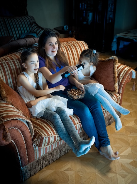 Portrait of mother and two daughters watching TV at night on sofa