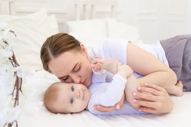 Portrait of a mother with a baby a mother gently embraces a child on a white bed at home maternal love and care