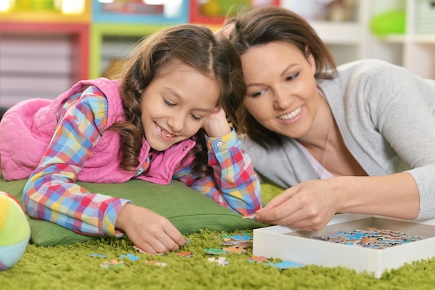 Portrait of mother with little daughter collecting puzzle