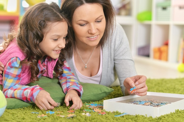 Portrait of mother with little daughter collecting puzzle