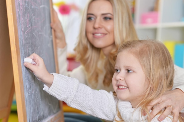 Portrait of mother with little daughter writing on blackboard