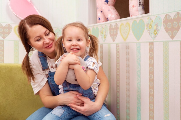 portrait of a mother with a smiling daughter in her arms, which hugs a soft toy