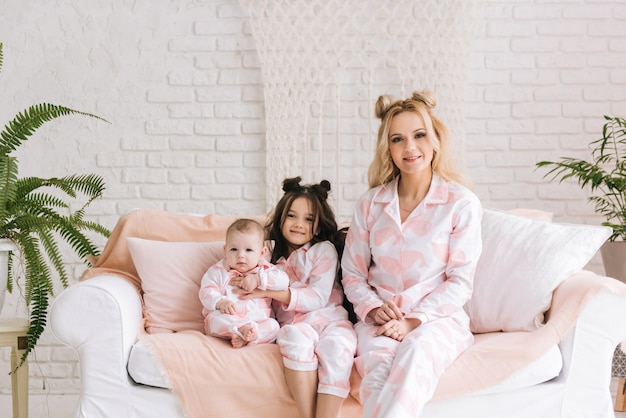 Portrait of mother with two daughters in the white room in the same pink pajamas, family look