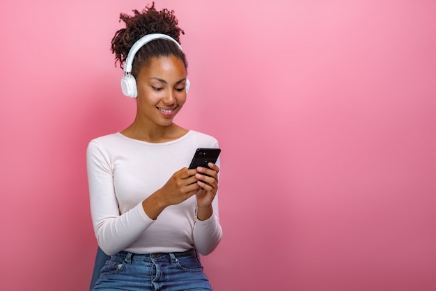 Portrait of a mulatto girl in earphones and holding a mobile phone looking at the screen