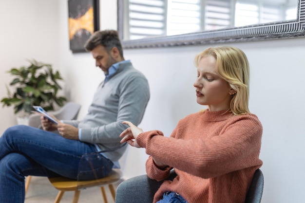 Portrait of multi ethnic group of people sitting in row on chairs while waiting in line at clinic copy space Woman checking time while man is reading an article