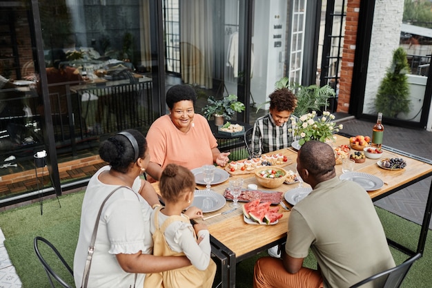 Портрет афроамериканской семьи из нескольких поколений, наслаждающейся званым ужином на открытом воздухе на террасе ...