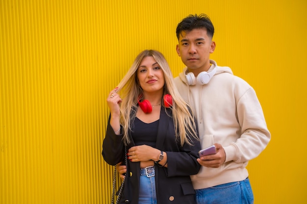 Portrait of multiethnic couple of asian man and caucasian woman on a yellow background smiling on university campus