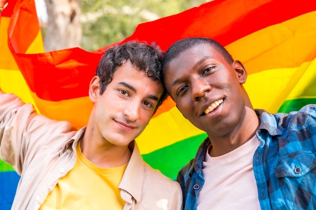 Portrait of multiethnic gay male couple holding a rainbow lgbt symbol flag romantic pose