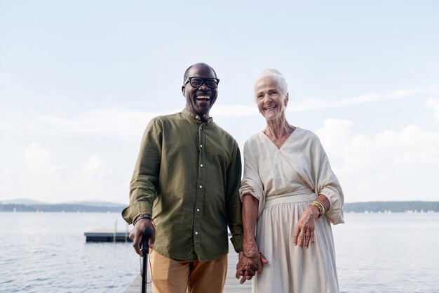 屋外に立ちながら手を繋ぎ、カメラに微笑む多民族の幸せな老夫婦のポートレート