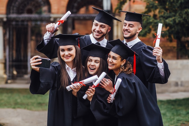 Photo portrait of multiracial graduates holding diploma and doing selfie on phone lifestule