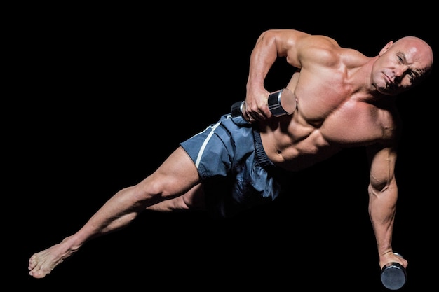 Portrait of muscular man exercising with dumbbells in side plank pose